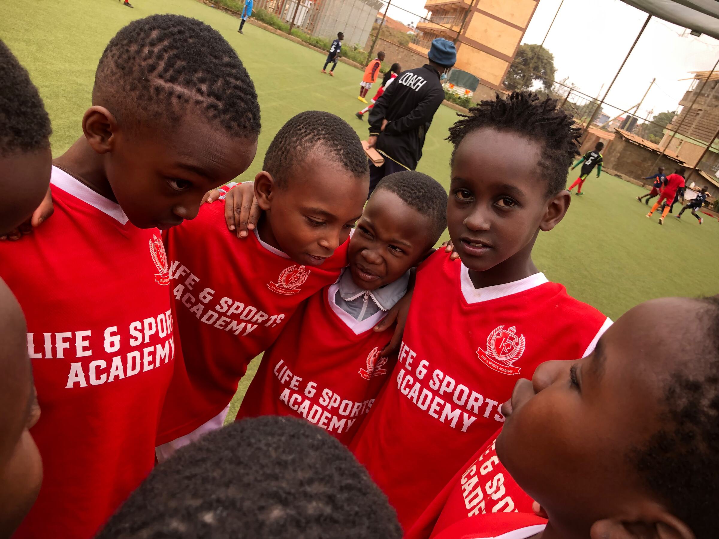 Life & Sports Academy players in red home shirts in a team huddle on the pitch